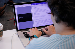 Over the shoulder view of person typing on a Mac laptop.