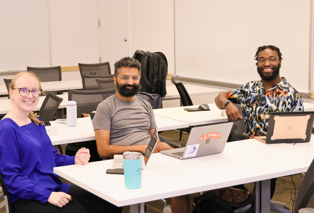 Three Summer Program participants sitting at a table and smiling at the camera
